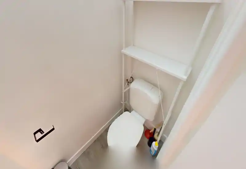 Compact, clean bathroom corner with a toilet, over-toilet shelving and cleaning supplies; bright white finishes and wood-effect flooring.