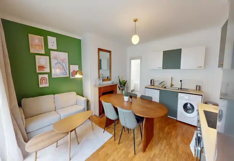 Bright, stylish open living area with a comfortable sofa, wooden coffee and dining tables, and an integrated kitchenette — tasteful decor and warm wood floors create a welcoming space.