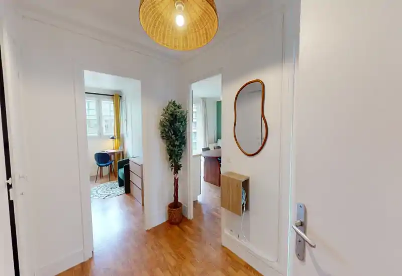 Bright, tidy entryway with wooden flooring, wall mirror and a small decorative shelf; the photo shows the apartment entrance and adjoining rooms.