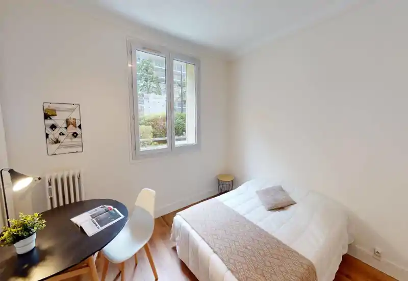 Chambre lumineuse et soignée avec lit blanc, textiles confortables et bureau près de la fenêtre — style minimaliste, idéal pour une personne.