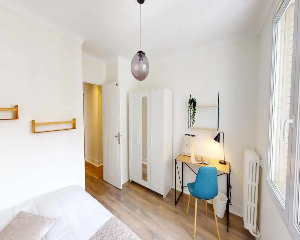 Camera da letto luminosa e moderna con letto visibile, armadio bianco e una piccola scrivania vicino alla finestra — arredo minimale e luce naturale.