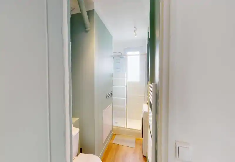 Compact modern bathroom with a shower enclosure, wall tiles and a slim towel radiator; clean, bright and efficiently arranged for small spaces.