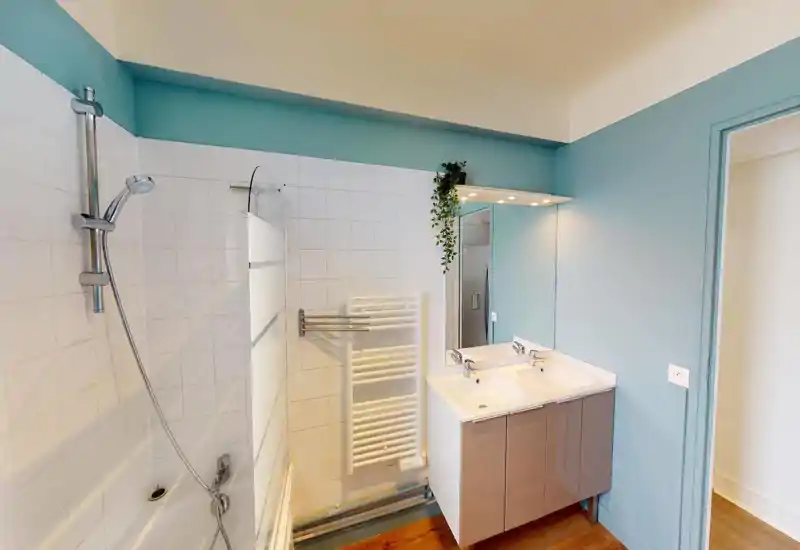 Bright modern bathroom with a bathtub and handheld shower, double sink vanity and large mirror; light teal walls and wooden floor add a fresh, contemporary feel.
