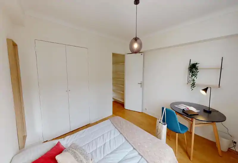 Camera da letto luminosa e minimal con letto doppio in primo piano, armadio a muro, una scrivania piccola e una lampada a sospensione — stile moderno e pavimenti in legno caldo.