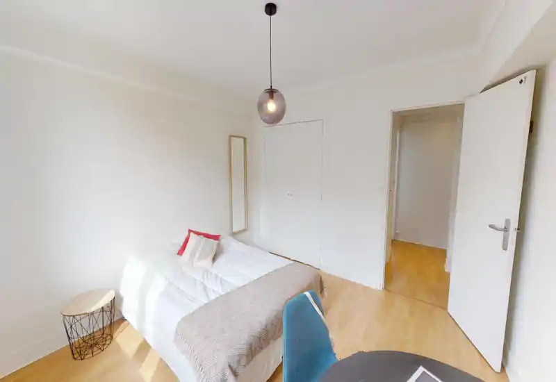 Camera da letto luminosa e minimal con letto matrimoniale ben rifatto, plaid e cuscini decorativi. Pavimento in legno chiaro, lampada a sospensione e armadio a muro danno un aspetto moderno e tranquillo, perfetto per un annuncio.