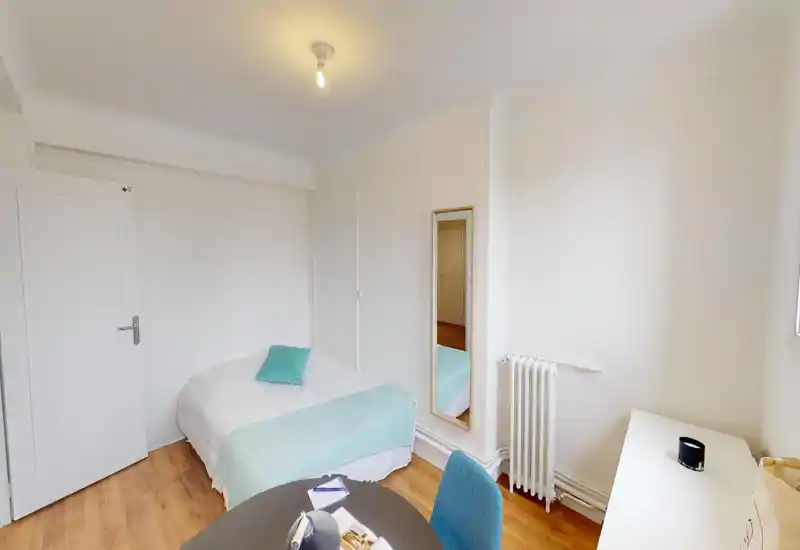 Chambre lumineuse et soignée avec un lit double en linge blanc et un plaid turquoise pâle, miroir pleine longueur et bureau simple — un espace calme et minimaliste pour se reposer.