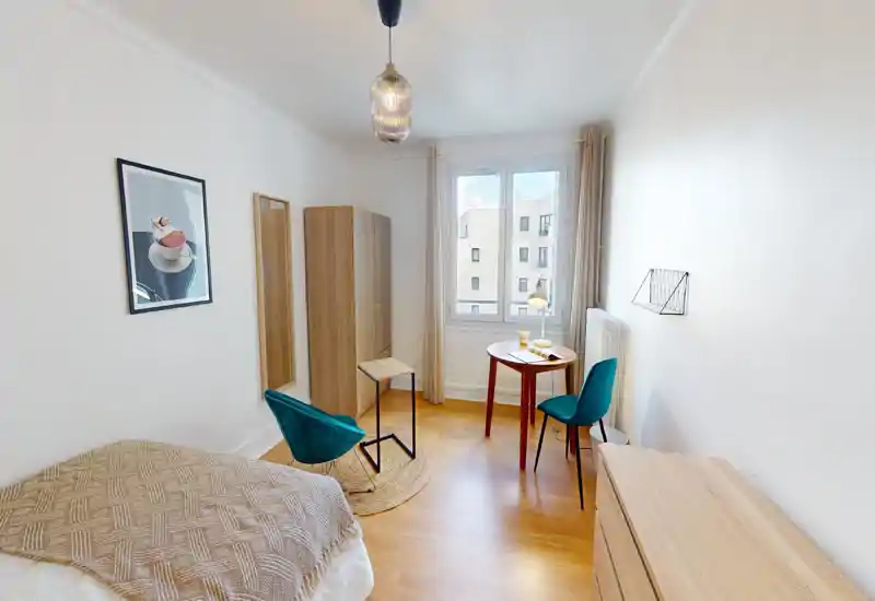 Bright, modern bedroom with a visible double bed, warm wooden flooring, a wardrobe and a small round table by the window — ideal for single or couple stays.