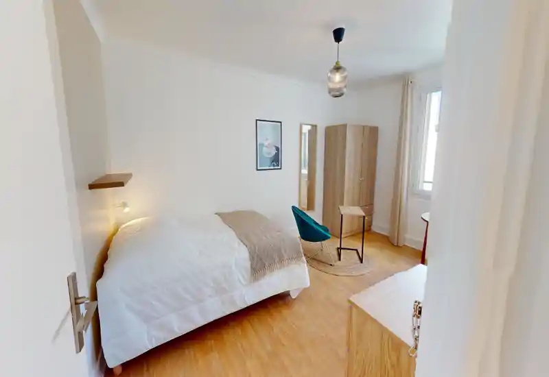 Bright, styled bedroom with a large bed, cozy throw and warm wooden furniture. The room features a wardrobe, mirror and a window that provides natural light.