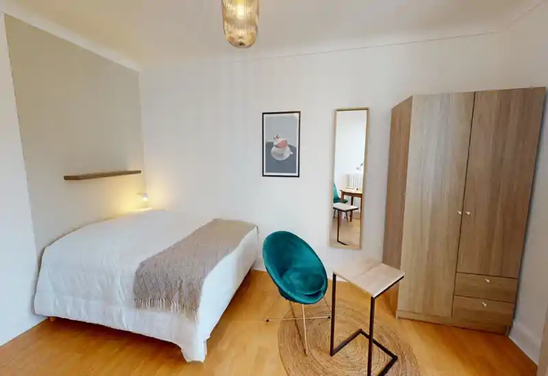 Bright, modern bedroom with a fully visible double bed, cozy throw blanket and warm wooden floors; includes a wardrobe, full-length mirror and a stylish teal accent chair.