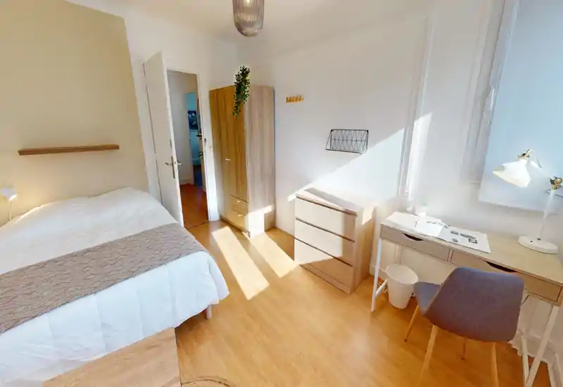 Bright, cozy bedroom with a double bed, wooden floor and simple modern furniture including a wardrobe, chest of drawers and a small desk by the window — ideal for restful stays.