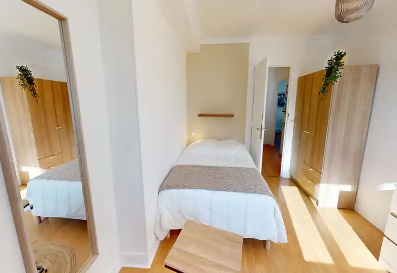 Bright, cozy single bedroom with a neatly made bed, warm wood wardrobes and natural light. Clean, minimal styling ideal for a rental listing highlighting comfort and storage.
