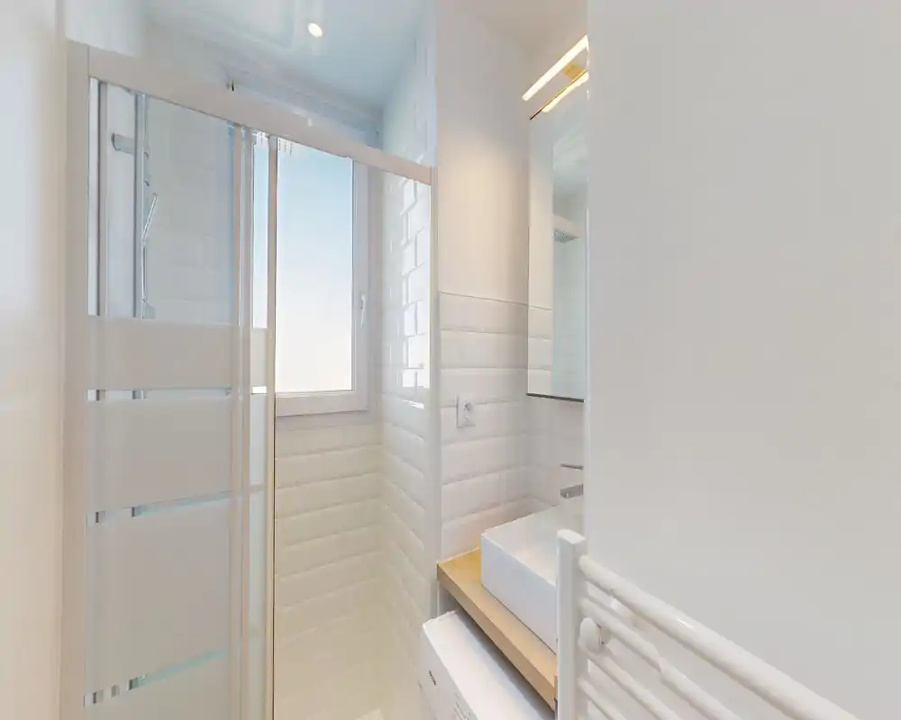 Bright, modern bathroom with white subway tiles, a glass shower enclosure, a countertop sink and a heated towel rail; compact and clean design with natural light from the window.