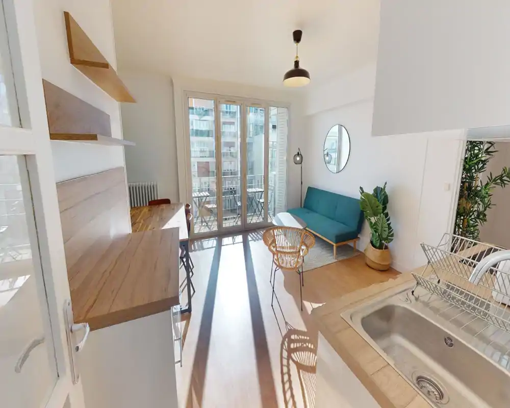 Bright, stylish living area with large floor-to-ceiling balcony doors, a teal sofa, rattan chair and wooden accents — ideal for relaxing or entertaining.