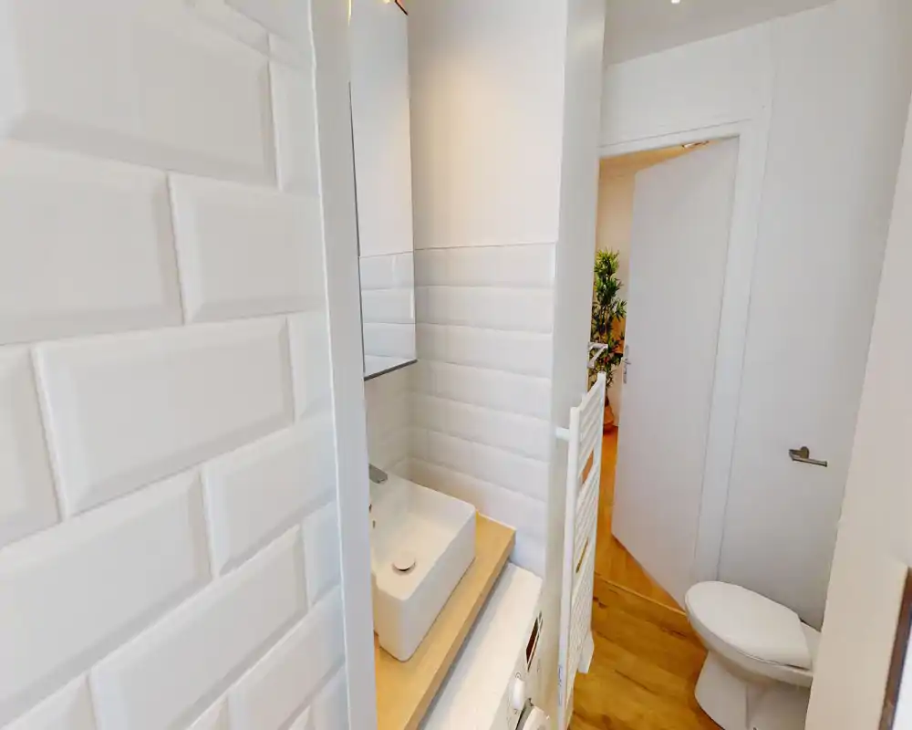 Compact modern bathroom with white subway tiles, a vessel sink on a wooden counter and a toilet; bright, clean finish ideal for short-term rentals.