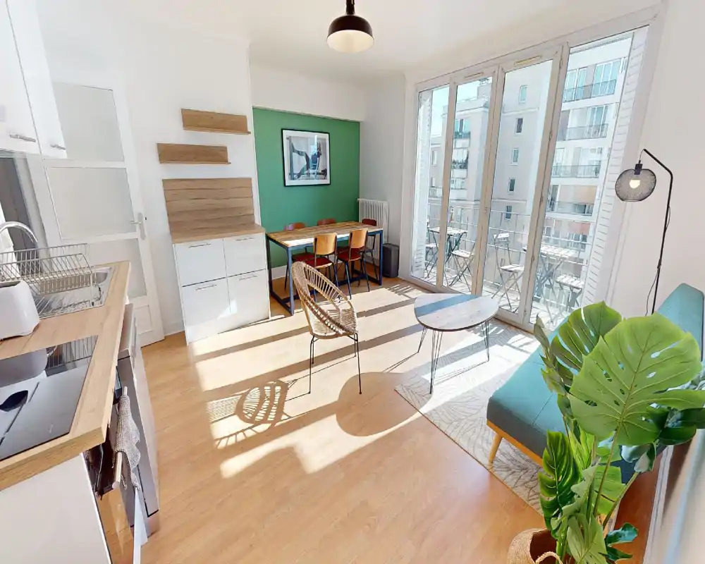 Bright, modern living area with large floor-to-ceiling windows, a compact kitchenette, dining table and cozy seating—ideal for a sunny city apartment.