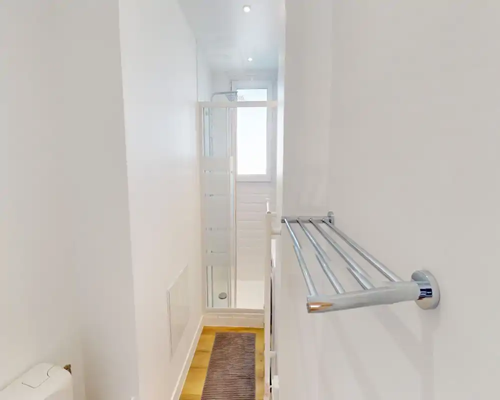 Bright, compact bathroom with a walk-in shower, glass sliding door, white tiles and a chrome towel rack; minimal and modern design.