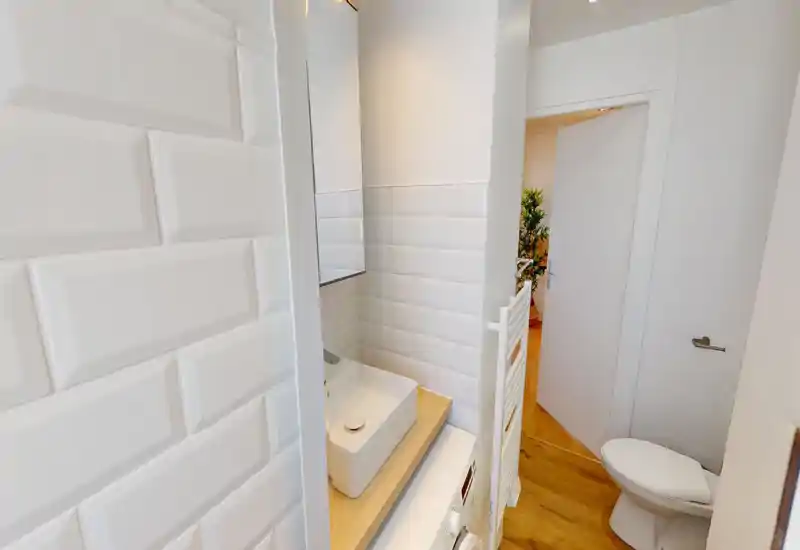 Compact modern bathroom with white subway tiles, a vessel sink on a wooden counter and a toilet; bright, clean finish ideal for short-term rentals.
