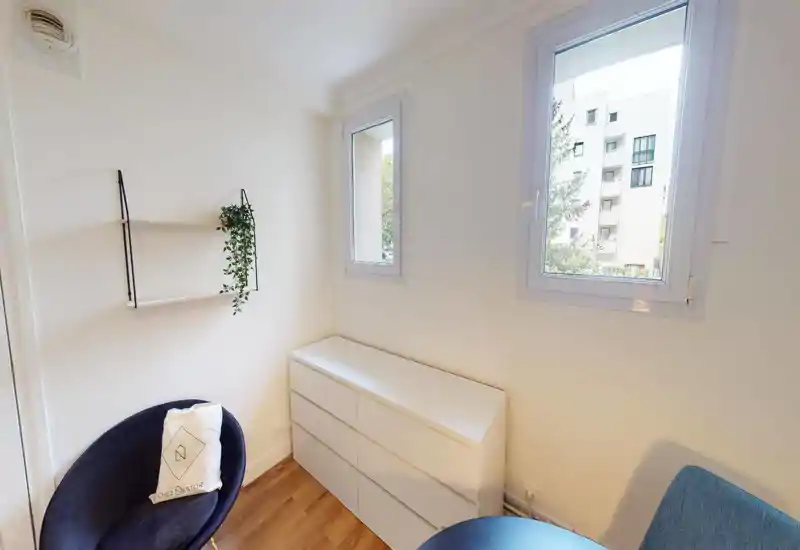 Camera da letto in mansarda con soffitto inclinato e pareti bianche luminose; un letto con cuscini è visibile in primo piano nonostante artefatti dell'immagine.