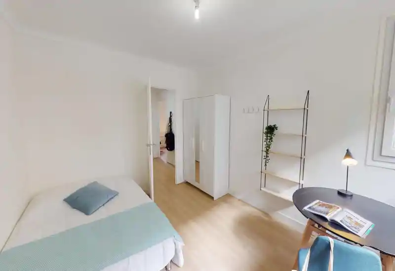 Bright, minimalist bedroom with a double bed, wardrobe and a small desk by the window. Light wood flooring and neutral walls create a calm, airy atmosphere ideal for rentals.