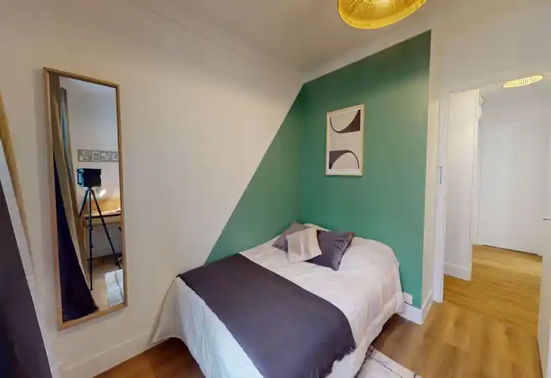 Piccola camera da letto accogliente con letto singolo appoggiato a una parete verde, cuscini decorativi e tessili morbidi; pavimento in legno caldo e illuminazione equilibrata creano un'atmosfera invitante.