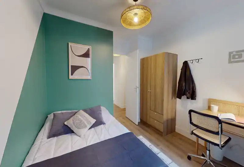 Camera da letto singola luminosa e accogliente con parete verde acqua, letto con cuscini e copriletto blu, armadio e scrivania compatta — perfetta per studenti o affitti singoli.