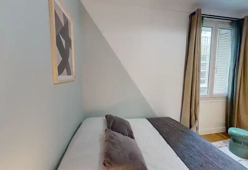 Camera da letto luminosa e arredata, con un grande letto contro una parete bicolore e luce naturale dalla finestra; tessili e cuscini neutri creano un’atmosfera accogliente.