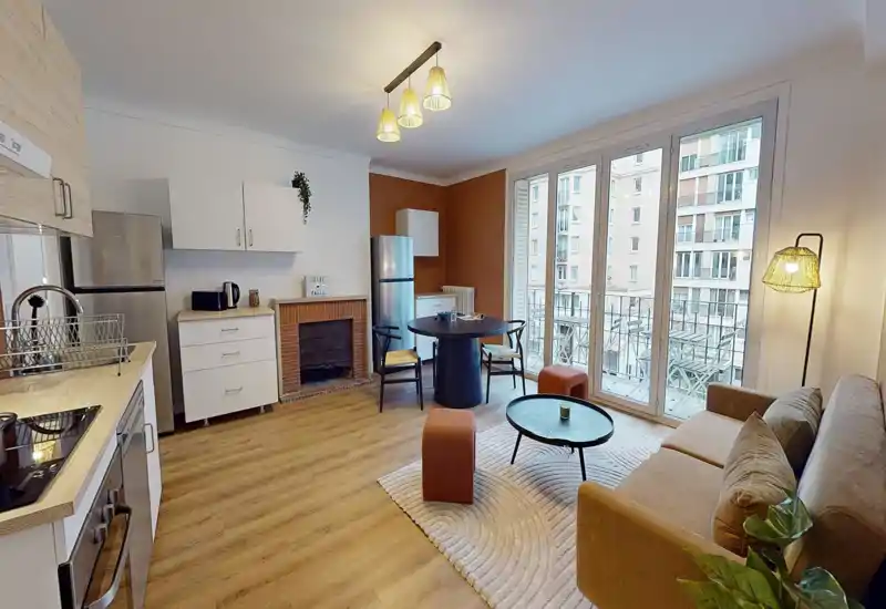 Bright, stylish living area with an open kitchenette, comfortable sofa, round dining table and large floor-to-ceiling windows offering plenty of natural light.