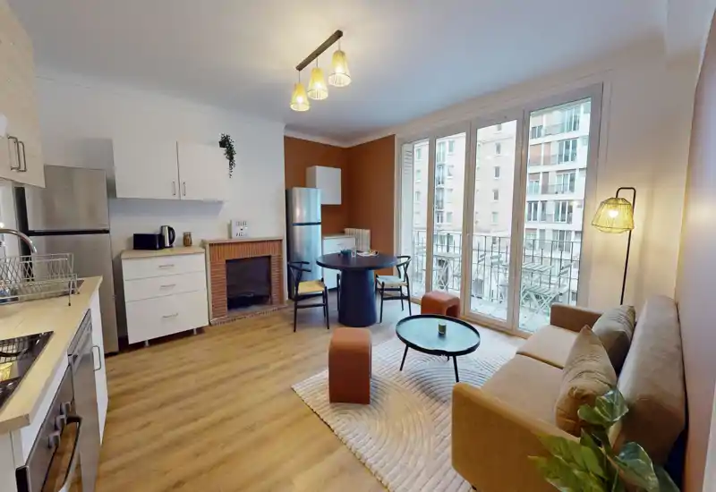 Bright, stylish open living area with a compact kitchenette, round dining table, comfortable sofa and large floor-to-ceiling windows that open to a balcony — ideal for city stays.