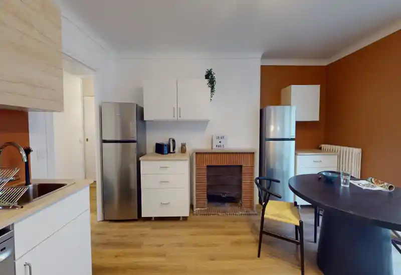 Bright, open-plan kitchen with wooden floors, stainless-steel appliances and a round dining table — warm accents and tidy styling ideal for a rental listing.
