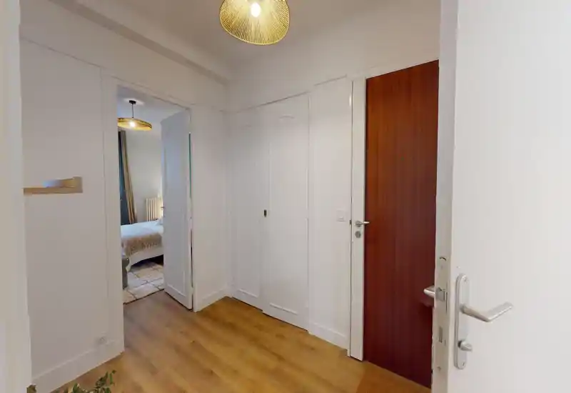 Bright, tidy apartment entrance with wooden floor, built-in closets and a view into a bedroom — welcoming first impression for guests.