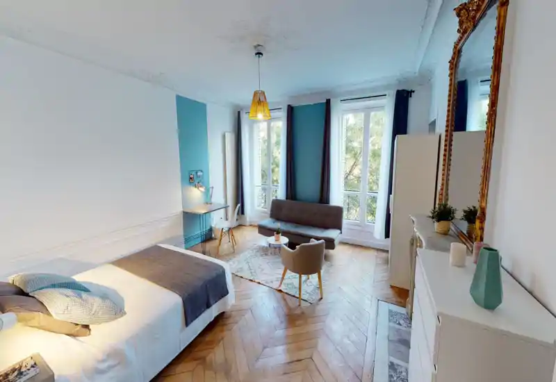Ampia e luminosa camera da letto con letto comodo, piccolo angolo salotto e grandi finestre che assicurano molta luce naturale. Pavimento in parquet classico e arredi curati creano un ambiente accogliente.