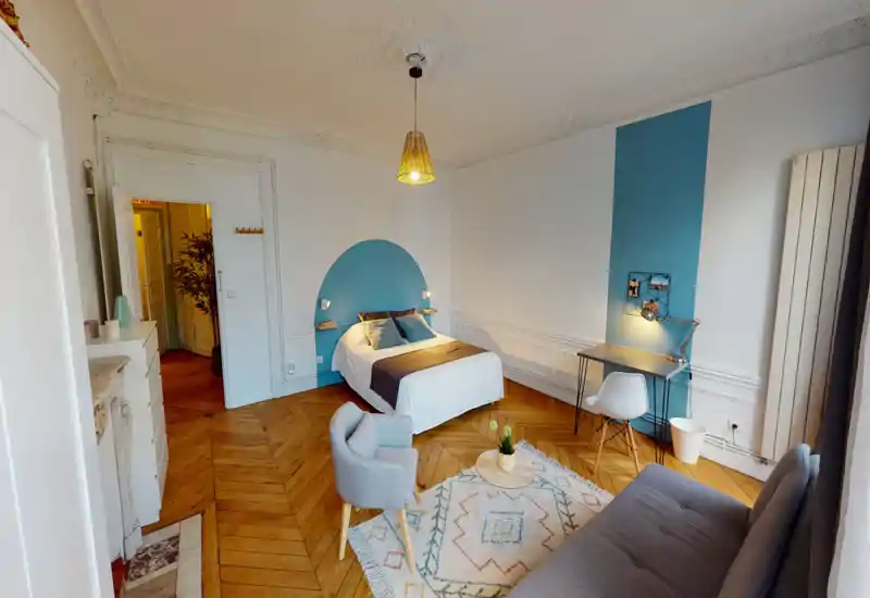 Camera da letto luminosa e di stile con letto matrimoniale centrato su una parete d'accento dipinta, pavimento in parquet caldo, comoda area salotto e una piccola scrivania — ideale per coppie o viaggiatori singoli.