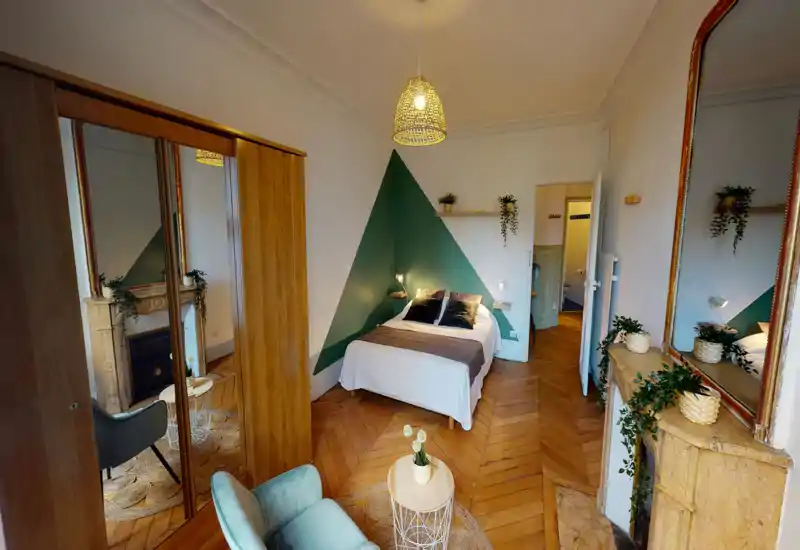 Chambre lumineuse et décorée avec goût, lit double placé devant un mur vert géométrique, parquet chaleureux, miroir décoratif et plantes apportant une ambiance cosy.