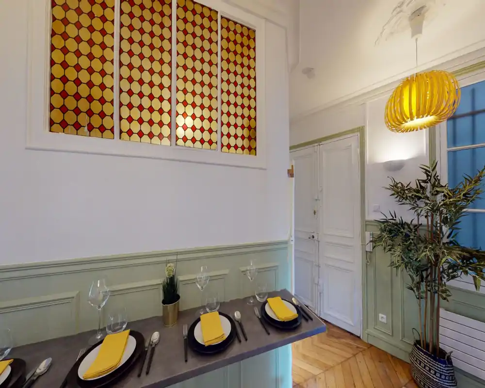 Coin repas lumineux et élégant avec bar aménagé : couverts et serviettes jaunes, suspension chaleureuse et plantes décoratives offrent un espace accueillant pour les repas.