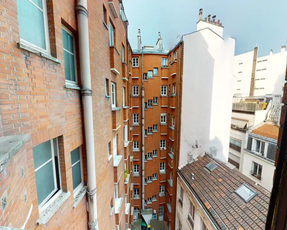 View of an inner-city courtyard and neighboring building facades with brick walls and rooftops, seen from a window. Good sharpness and natural daylight highlight architectural details.