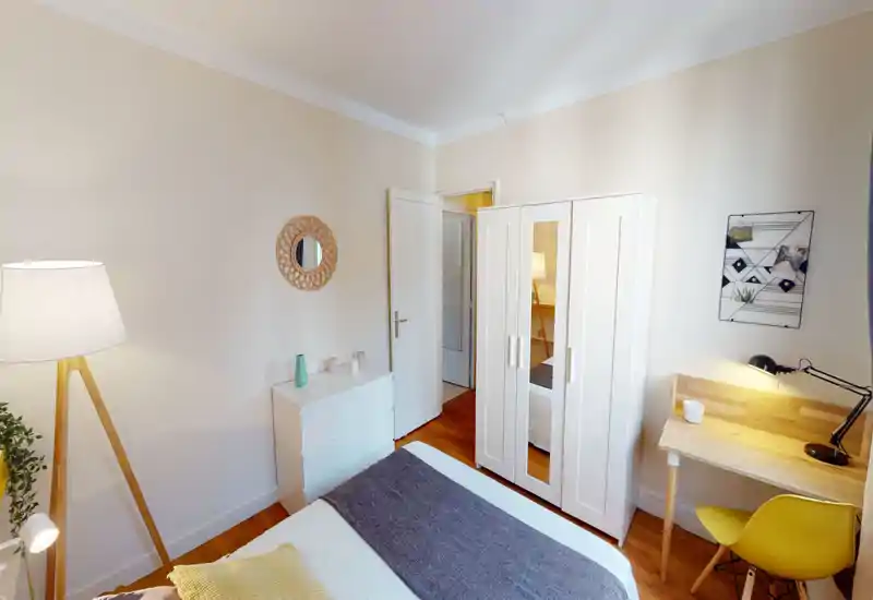 Chambre lumineuse et chaleureuse avec lit bien fait, armoire blanche à panneau miroir, petit bureau en bois et éclairage d'ambiance — parfaite pour une annonce locative.