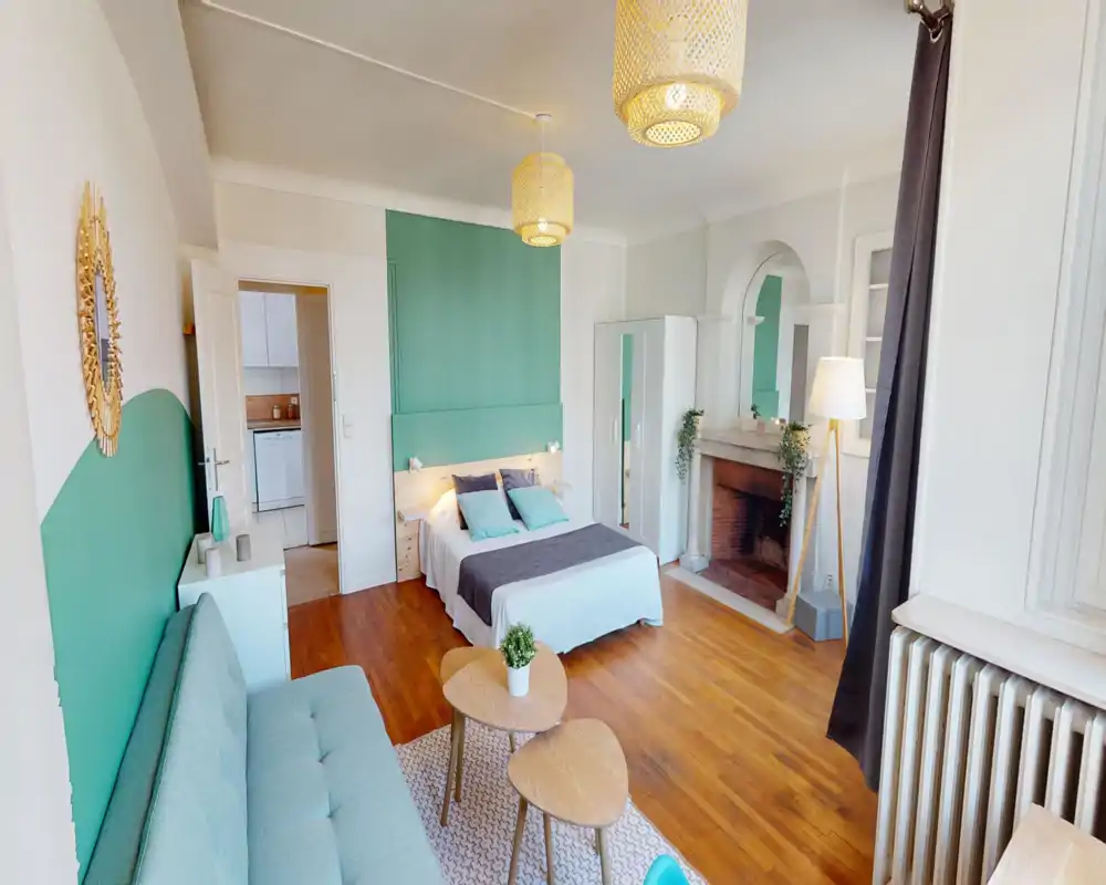 Chambre lumineuse et élégante avec lit double, textiles accueillants et petit coin salon; parquet et mur vert apportent une atmosphère chaleureuse et contemporaine.