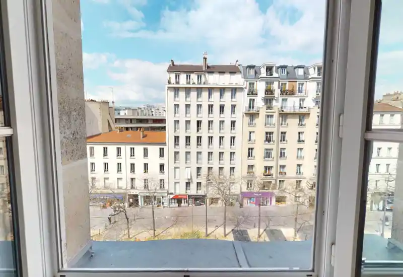 Vue dégagée sur la rue depuis une grande fenêtre, avec immeubles résidentiels et ciel bleu — parfaite pour valoriser l’orientation de l’appartement.