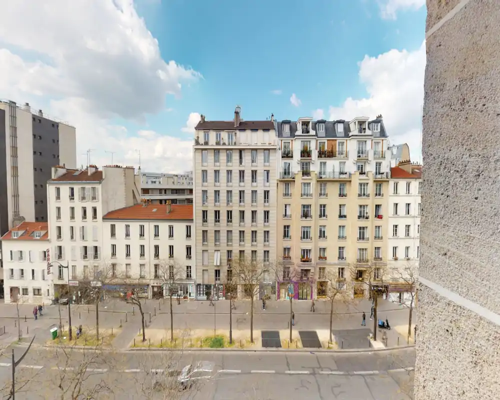 Street-facing view from an exterior opening showing a row of multi-storey residential buildings, trees and a road — ideal for listing a balcony or window view.