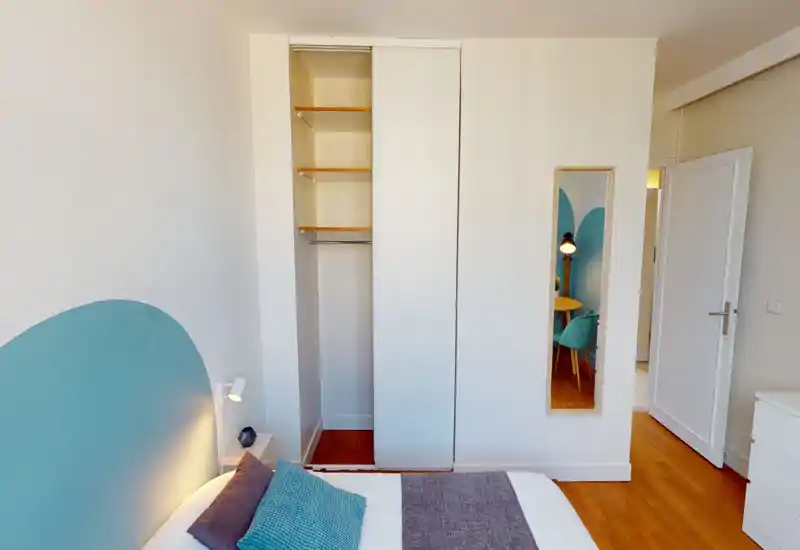 Bright, neatly staged bedroom with a visible bed, teal headboard and soft textiles. Clean built-in wardrobe with sliding doors and wooden floors create a warm, modern look.