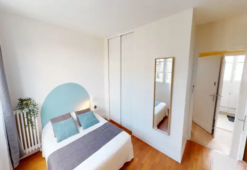 Bright, well-staged double bedroom with wooden floors, a painted semicircle headboard, and large built-in wardrobe. Natural light from the window and soft textiles create a cozy, inviting atmosphere.