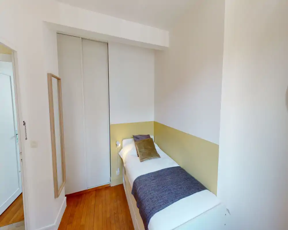 Camera da letto singola luminosa e ordinata con letto bianco, fascia colorata a parete e pavimento in legno — perfetta per un affitto compatto e tranquillo.