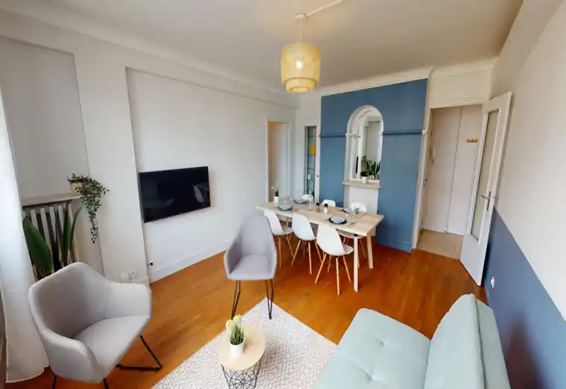 Bright, well-staged living room with a sofa, armchairs, wall-mounted TV and a dining table; modern Scandinavian-style décor with wooden floors and plants.