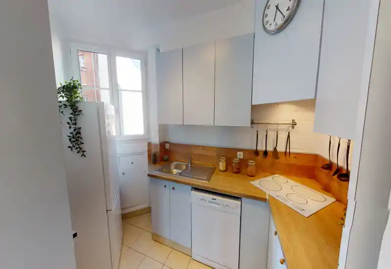 Compact, bright kitchen with wooden countertops, white cabinets, a sink, dishwasher and hanging utensils — well-lit by a window and under-cabinet lighting.