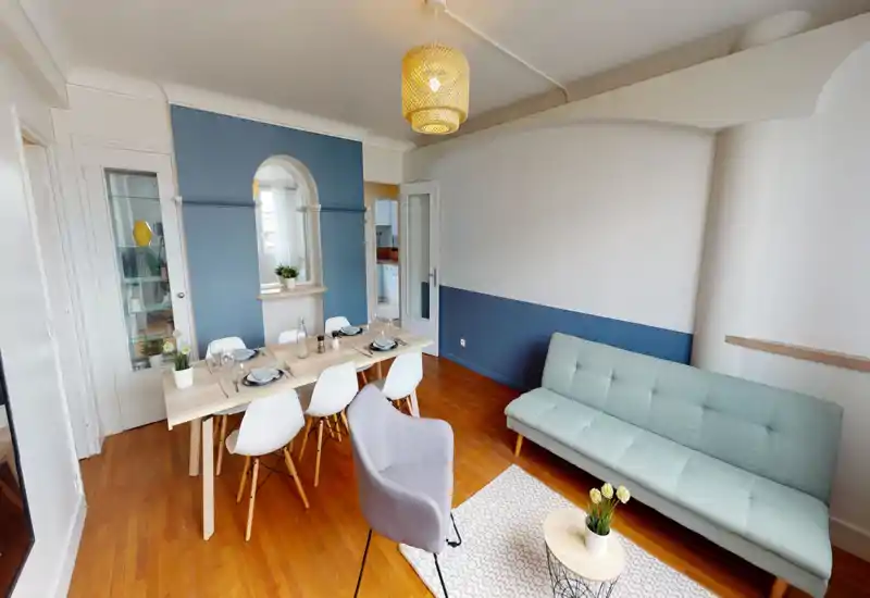 Espace séjour/salle à manger lumineux et moderne avec une table en bois clair dressée pour quatre, un canapé vert menthe et des accents décoratifs soignés pour une atmosphère accueillante.