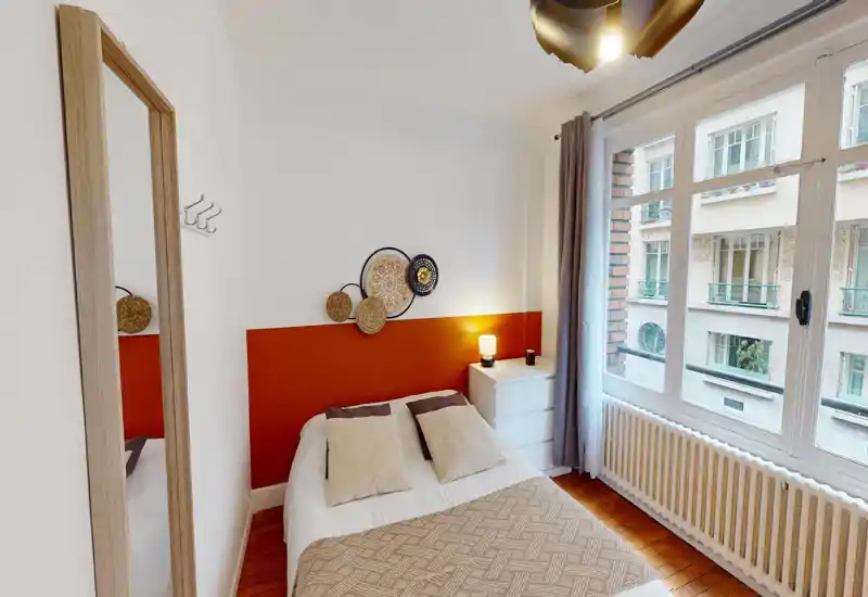 Image corrompue mais chambre identifiable : lit double avec tête de lit, oreillers et textiles, près d'une fenêtre ; bonne lumière naturelle malgré les artefacts.