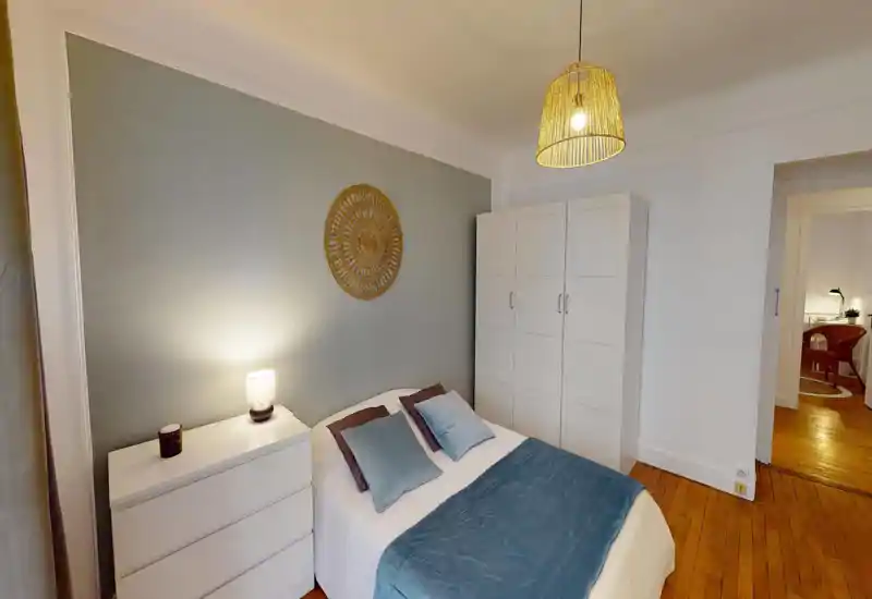 Bright, cozy double bedroom with a neatly made bed, decorative wall art, wardrobe and chest of drawers. Warm pendant light and bedside lamp create a comfortable atmosphere ideal for restful stays.