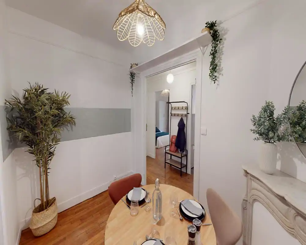 Coin repas lumineux et soigné avec une table ronde en bois dressée pour quatre, des plantes décoratives et un parquet chaleureux.