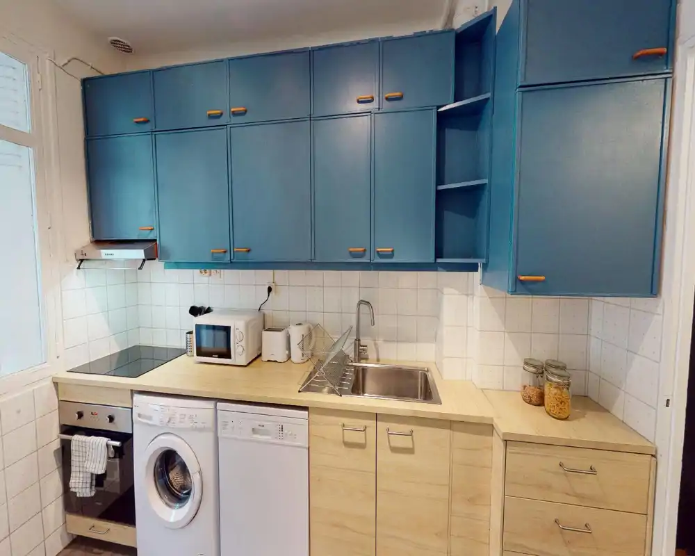 Cuisine compacte identifiable malgré les distorsions numériques : plan de travail, évier et appareils intégrés visibles ; tons clairs et finitions modernes perceptibles.