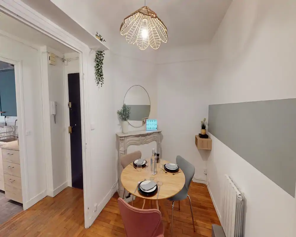 Coin repas chaleureux et aménagé avec une table ronde en bois pour quatre, chaises colorées, miroir décoratif et suspension lumineuse — idéal pour mettre en valeur un coin repas compact.